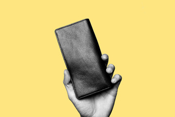 Concept of modern man, searching for money, save money, leather accessories. Hand holding a black long leather wallet. Black and white subject with yellow background. Top copy space