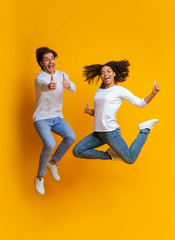 Fototapeta na wymiar Excited Multiracial Couple Jumping And Gesturing Thumbs Up, Having Fun Together