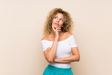 Young blonde woman with curly hair over isolated background thinking an idea while looking up