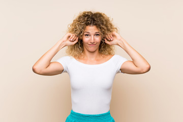 Young blonde woman with curly hair over isolated background frustrated and covering ears