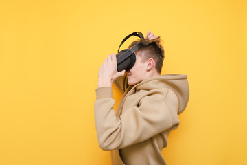 Guy in casual clothes wears a VR helmet and is about to play video games isolated on a yellow background. Young man testing a virtual reality helmet. VR gaming concept