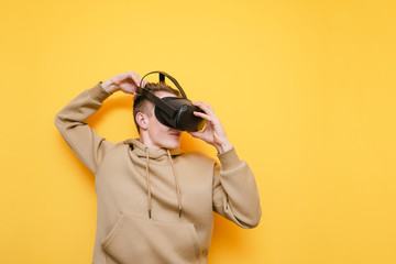 Guy in casual clothes wears a VR helmet and is about to play video games isolated on a yellow background. Young man testing a virtual reality helmet. VR gaming concept