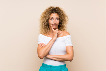 Young blonde woman with curly hair over isolated background Looking front