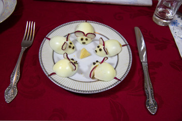 Eggs on a white plate in the form of mice with ears of radish, eyes of black pepper peas on a background of cherry tablecloth table items. Food, original dishes, products.
