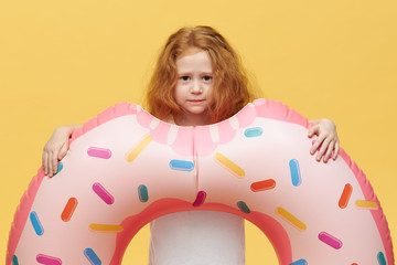 Obraz na płótnie Canvas Isolated shot of charming little girl with long voluminous hair posing in studio with rubber ring going to have swim in sea during vacations. Pretty female child holding swimming inflatable circle