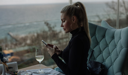 Luxury woman using mobile phone in restaurant with sea view