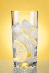 glass of cold water with ice and lemon on a yellow background