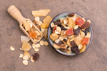 Muesli with dried fruits in a bowl on a brown textured background, empty copy space, healthy...