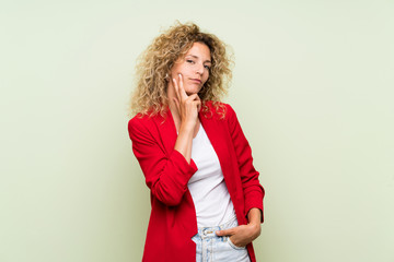 Young blonde woman with curly hair over isolated green background thinking an idea while looking up