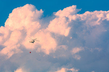 Helicopter with bucket full of water in a sky
