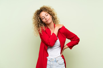 Young blonde woman with curly hair over isolated green background suffering from pain in shoulder for having made an effort