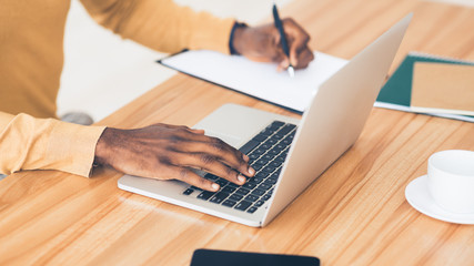 Unrecognizable black guy working on his laptop and writing