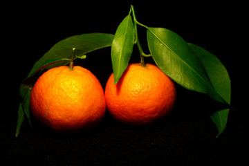 two tangerines with green leaves up isolated on black