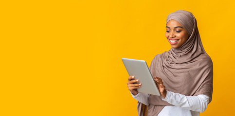 Smiling black islamic girl in hijab using digital tablet