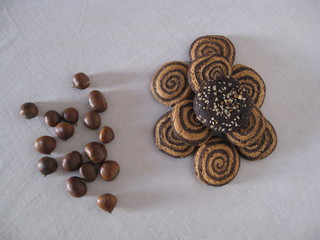 galletas de algarroba artesanas, ecológicas, con dibujo de espiral y distintos tipos  apiladas junto a conjunto de castañas crudas. Frutos y dulces de temporada, otoño invierno