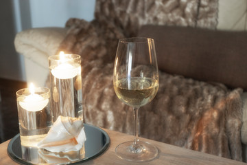 Wine glass on wooden table in living room, cosy sofa and warm blanket int the back. Relax at home...
