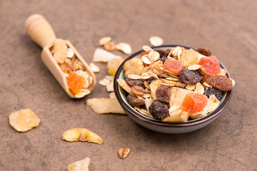 Muesli with dried fruits in a bowl on a brown textured background, empty copy space, healthy breakfast
