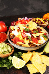 mexican nacho chips garnished with ground beef, guacamole, melted cheese, peppers and cilantro leaves in plate