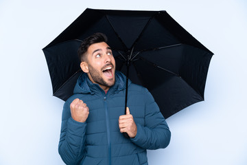 Man holding an umbrella over isolated background celebrating a victory