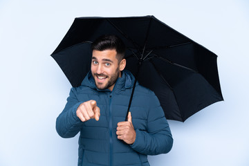 Man holding an umbrella over isolated background points finger at you with a confident expression
