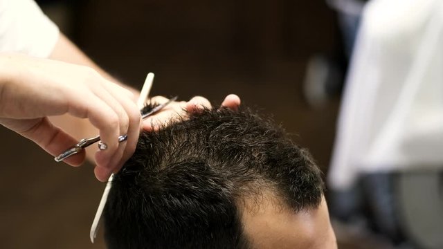 A client has black hair. A barber is using scissors. The men are in the salon.