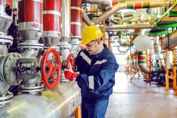 Hardworking handsome caucasian plant worker in protective suit and with helmet on head trying to...