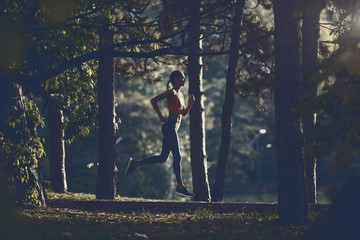 Side view of slim attractive caucasian brunette in sportswear and with ponytail running on trail in woods.