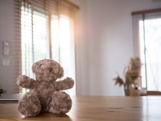 Teddy bear toy sit on the wood table in house , the sunlights through wood blind behind .Space for Text.