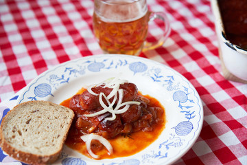 Czech food specialty, roasted small sausages in beer sauce made from dark beer, tomato sauce, chily, garlic and onion served on rustic plate with glass of lager beer and bread, typical czech pub snack