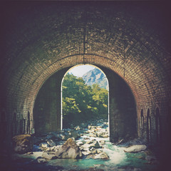 Digital photo manipulation of an alpine mountain stream running through an old arched brick tunnel. Nature and wilderness meet vintage architecture. Portal into another world concept.
