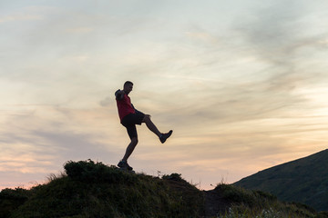 Fototapeta na wymiar Dark silhouette of a hiker balancing on a summit stone in evening mountains.