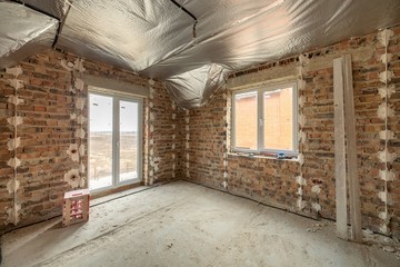 Interior of unfinished brick house with concrete floor and bare walls ready for plastering under construction. Real estate development