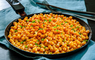 Fried spicy chickpeas in frying pan on wooden table.