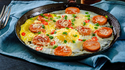 fried eggs with sausage and cheese in a frying pan on wooden table