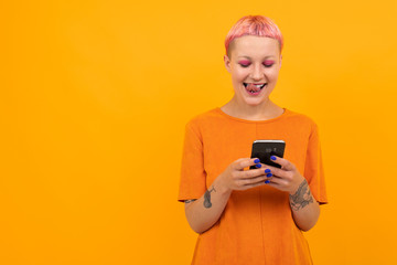 Extraordinary beautiful woman with short pink hair and big tattoo on her hand smiles isolated on orange background