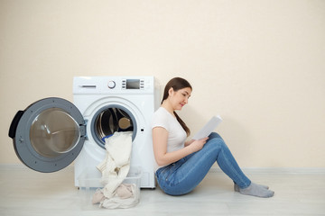 young housewife in jeans learns settings of new washing machine with instruction sitting on floor copy space