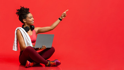 Smiling fitness girl with laptop pointing up at copy space