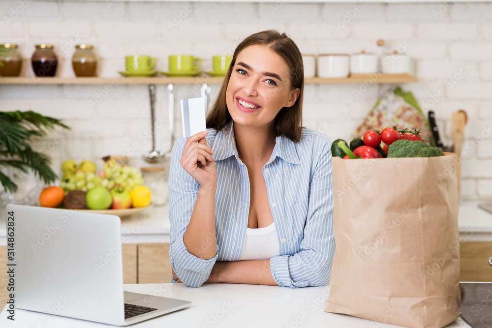 Wall mural Online groceries. Happy woman shopping with laptop in kitchen