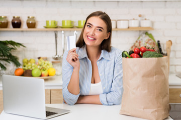 Obraz na płótnie Canvas Online groceries. Happy woman shopping with laptop in kitchen