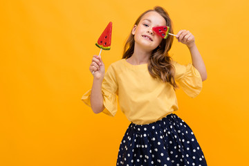 attractive caucasian young girl in a skirt and t-shirt with two watermelon lollipops on a yellow background