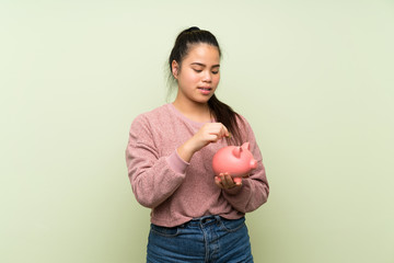 Young teenager Asian girl over isolated green background holding a big piggybank