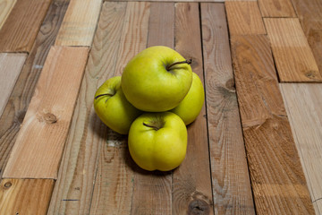 Four green apples stacked on a wooden board shot from the front in front of a window using normal daylight on a drizzly Sunday morning