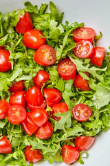 Red halved cherry tomatoes with fresh green arugula (rucola) leaves, closeup. Vegetable salad, top view