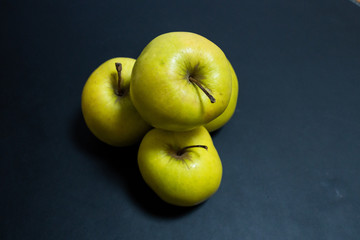 Green apples stacked upon each other against a black background shining due to daylight cascading through the kitchen window