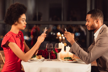 African American Couple Using Mobile Phones Having Date In Restaurant