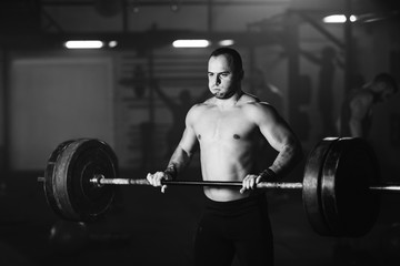 Fototapeta na wymiar Muscular build man making an effort while exercising with barbell in a gym.