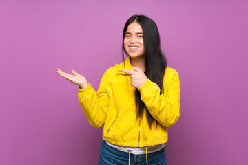 Young teenager Asian girl over isolated purple background holding copyspace imaginary on the palm to insert an ad