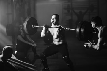 Fototapeta na wymiar Muscular build man shouting while lifting barbell in health club.