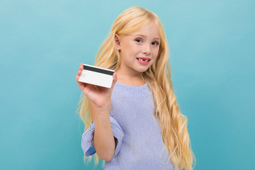 Portrait of little caucasian girl in blue t-shirt with long blonde hair holds a credit card isolated on blue background