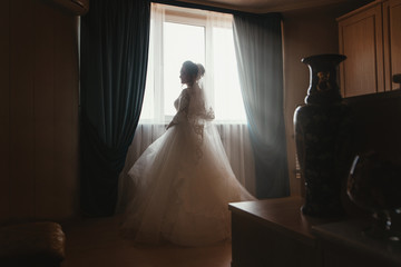Silhouette of a beautiful bride in a traditional white wedding dress in front window.